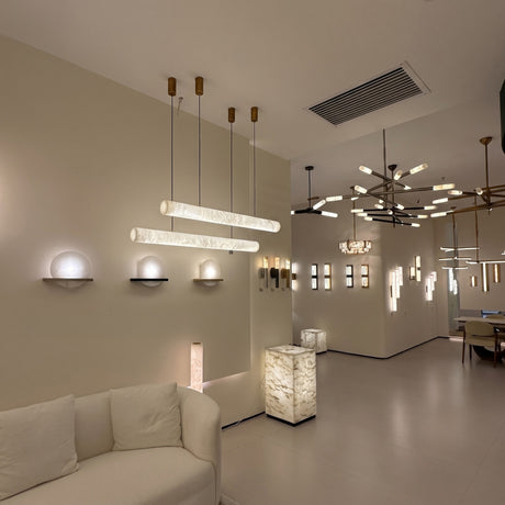 Zareon LED Large Linear Alabaster Chandelier in soft white, shown as two cylindrical pendants on slim cables above a showroom seating area with warm ambient glow.