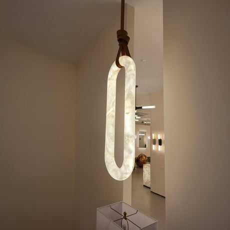 Serava Large LED Alabaster Pendant Light in Soft White, an elongated capsule-shaped fixture with copper leather strap detail, glowing softly in a hallway setting.