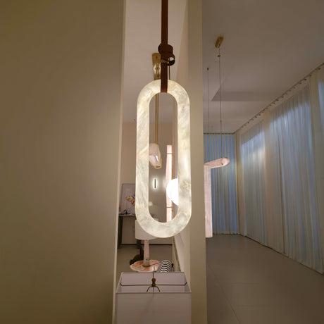 Serava Small alabaster pendant light with elongated rounded form and brown leather strap detail, shown glowing warm white in a hallway setting.