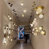 Serano Travertine Disc Wall Light in light beige stone with off-centre opal glass globe, shown mounted in a lit showroom display among other pendant and wall lights.