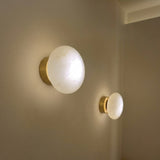 Solenne LED Halo Alabaster Wall Light in Brushed Brass, domed stone discs glowing warmly on a brass backplate, shown as a pair mounted on a wall near a doorway.