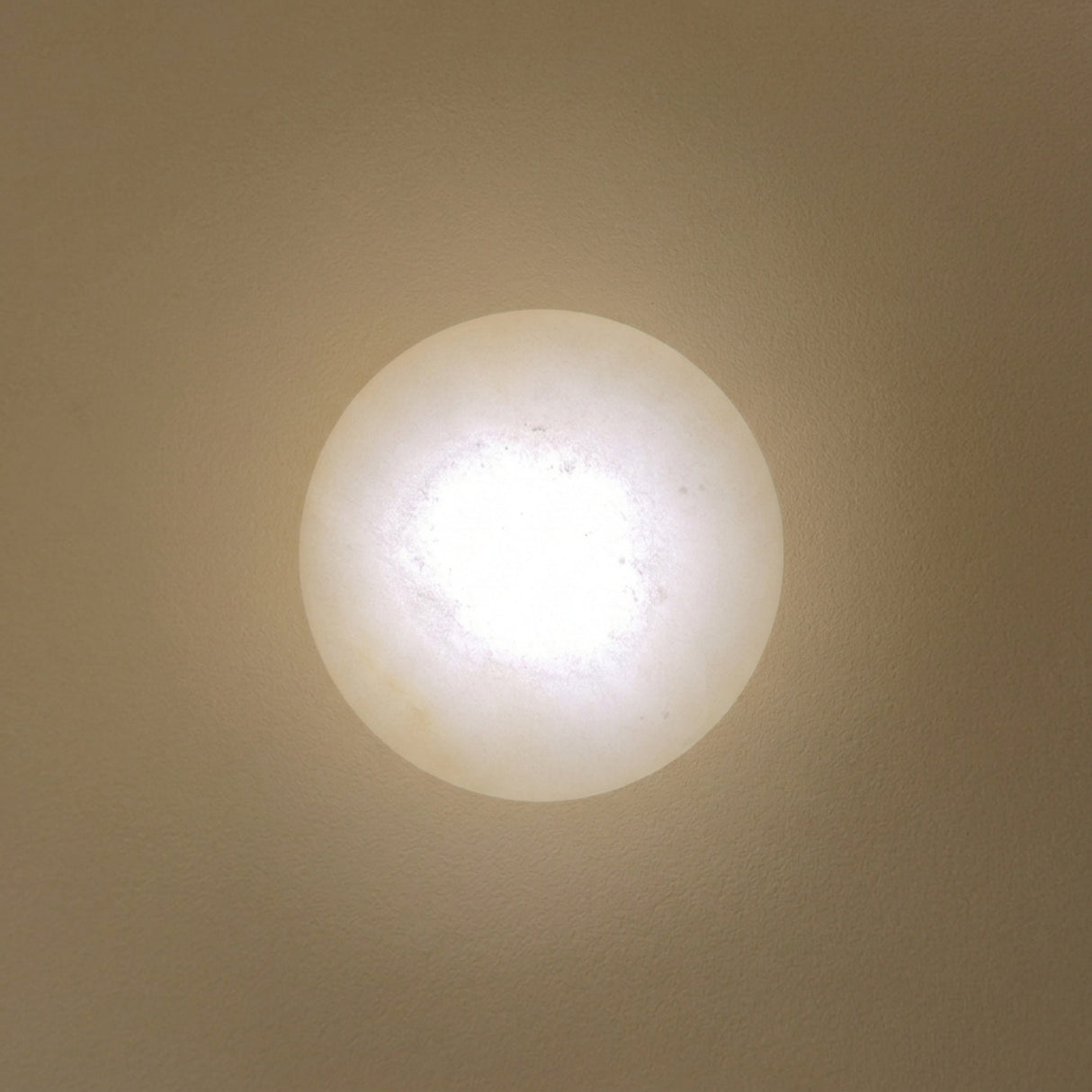 Solenne LED Halo wall light with a round domed alabaster disc glowing warm white, set on a brushed brass circular backplate against a neutral wall.