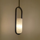 Eliona Capsule Alabaster Pendant Light in matt black, a single cylindrical alabaster shade lit warmly within an oval capsule frame, shown against a neutral wall.