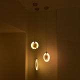 Luna LED Alabaster Disc Pendant Light 200mm in brushed brass, shown lit alongside similar pendants, illuminating a dim hallway with warm glowing light.