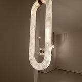 Serava Large LED Alabaster Pendant Light in Soft White, elongated capsule form with copper leather strap detail, glowing warmly in a modern living room setting.