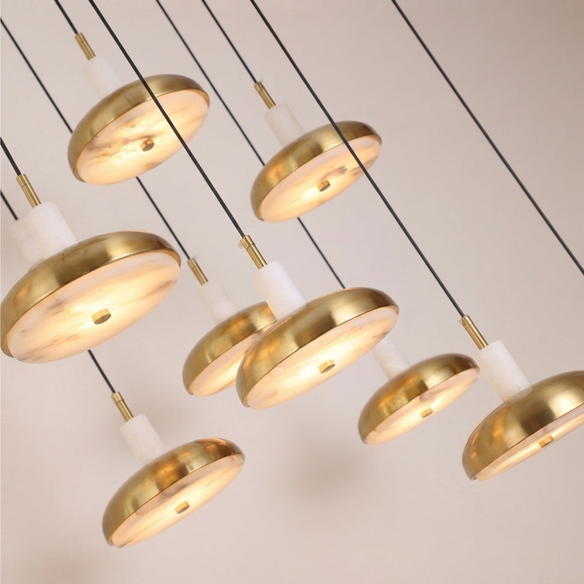 Aurevia 14-light LED linear chandelier in brushed brass with domed brass discs and staggered white alabaster cylinders, glowing warm white against a light background.