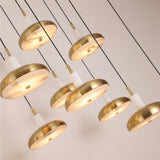 Aurevia 14-light LED linear chandelier in brushed brass with domed brass discs and staggered white alabaster cylinders, glowing warm white against a light background.
