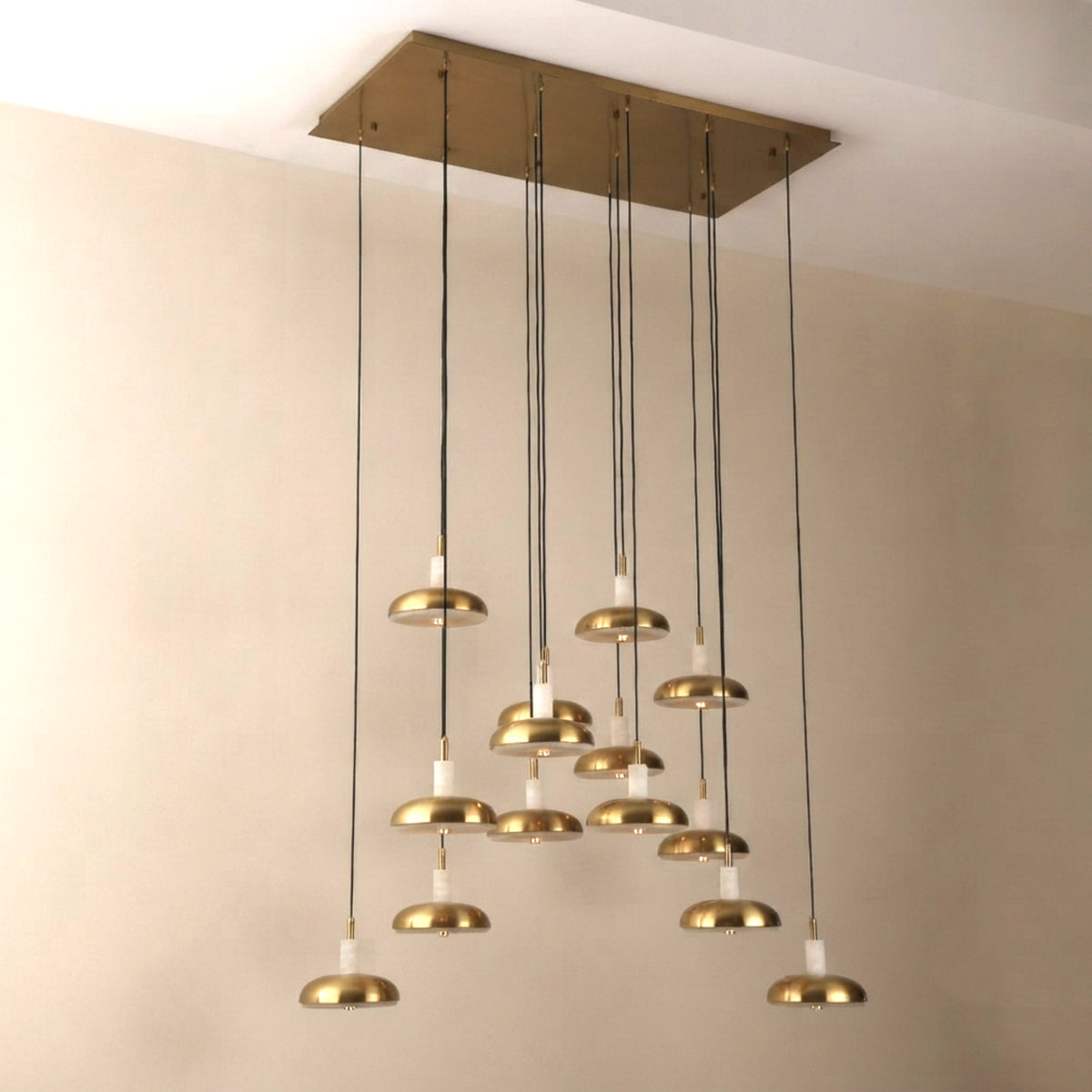 Aurevia 14-light LED linear chandelier with rectangular brushed brass canopy and staggered alabaster-and-brass domed drops, shown against a plain light wall.