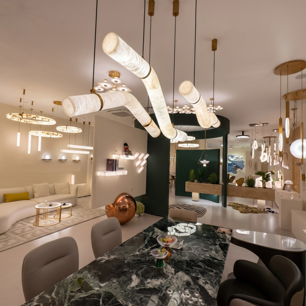 Zareon LED Medium Curved Alabaster Chandelier with S-shaped stone tubes and brushed brass collars, shown suspended above a dining table in a showroom setting.