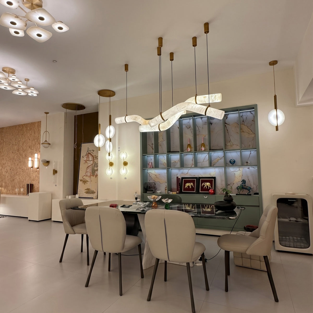 Zareon LED curved alabaster chandelier with brushed brass collars and canopies, shown above a dining table in a modern living room setting.