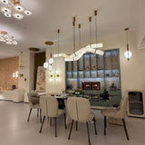 Zareon LED curved alabaster chandelier with brushed brass collars and canopies, shown above a dining table in a modern living room setting.