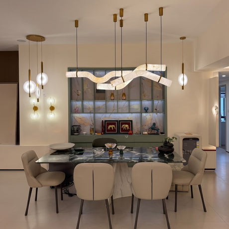 Zareon LED curved alabaster chandelier with brushed brass collars and canopies, shown above a marble dining table alongside globe pendant lights in a modern dining room.