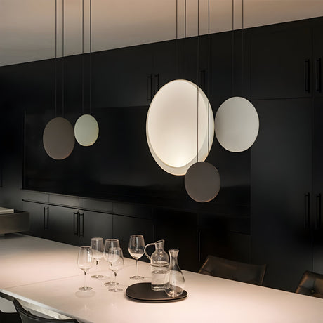 A modern dining area features a minimalist look with the Cosmos 3 Light LED Bar Pendant - V1, black cabinetry, and a white table set with glasses, a carafe, and a tray. The design is sleek, contemporary, and stylish.
