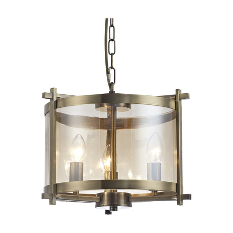 Nolan 3 Light E14 Pendant Light, 36cm drum-style fitting in antique brass with clear glass panels, three exposed candle bulbs and a suspending chain, shown on a plain white background.