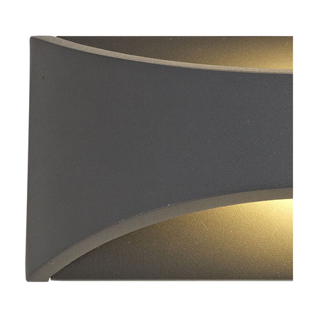 Close-up of the Aryana 22cm outdoor wall light in anthracite aluminium, showing the curved diffuser slots with warm white LED glow visible top and bottom.