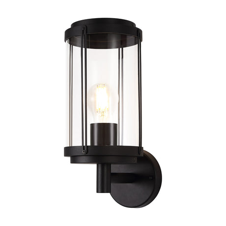 Reva E27 IP44 wall light in black, featuring a cylindrical clear polycarbonate shade with vertical bars, an exposed bulb, and a black mounting bracket on a plain white background.