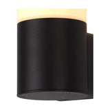 Prado E27 IP44 wall light in black, close-up of the cylindrical aluminium body with opal white shade lit warm, mounting plate visible, plain white background.