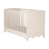 Dancer Convertible Cot Bed in cashmere tone with vertical slatted sides, scalloped bottom edge, and solid end panels, shown on a plain white background.