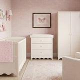 Dancer Changing Table with Drawers & Removable Top in cashmere finish, shown with three drawers and scalloped base in a pink nursery beside a matching cot and wardrobe.