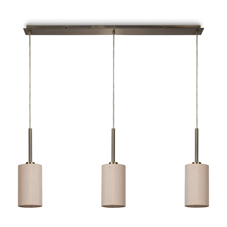 Baymont 3-light pendant with slim antique brass linear bar and cables suspending three narrow nude beige fabric drum shades, shown on a plain white background.