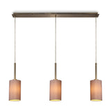 Baymont 3 Light Pendant Light with slim antique brass bar and three taupe fabric drum shades on cords, shown lit against a plain white background.