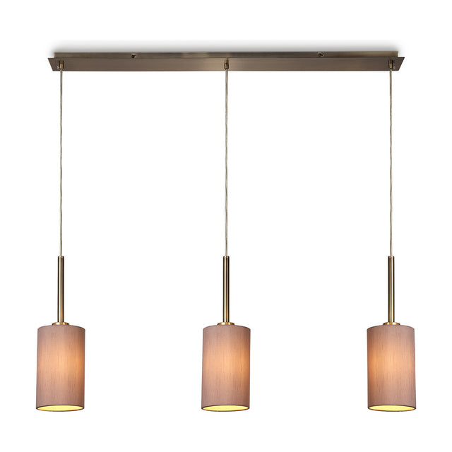 Baymont 3 Light Pendant Light with slim antique brass bar and three taupe fabric drum shades on cords, shown lit against a plain white background.