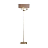 Banyan 3 Light E14 floor lamp with a slim antique brass column and wide grey faux silk drum shade housing three candle-style lights, on a round base against a plain white background.