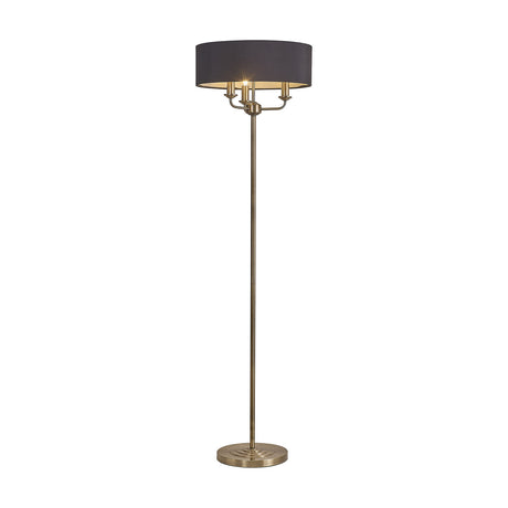 Banyan 3 Light E14 floor lamp with antique brass stem and curved arms holding candle bulbs beneath a wide black drum shade, round brass base, plain white background.
