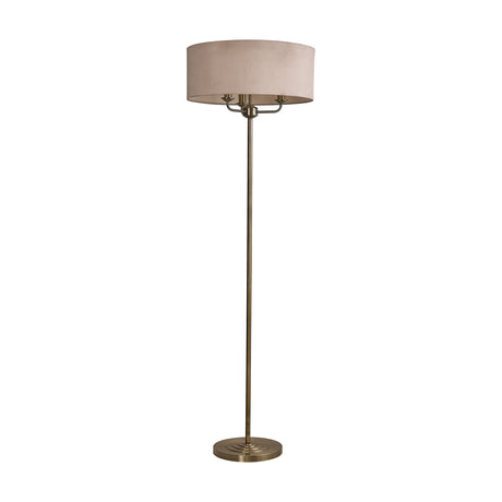 Banyan 3 Light E14 Floor Lamp with a wide drum shade in nude beige fabric atop a slim antique brass stem and round base, shown on a plain white background.