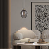 Cawdor E27 wine glass pendant light in smoke glass with antique brass fitting, 25cm shade, hung above a beige sofa in a living room setting.