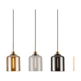 Three individual glass cylinder pendant lights with antique gold fittings, shown in amber, clear, and smoke finishes against a plain white background.