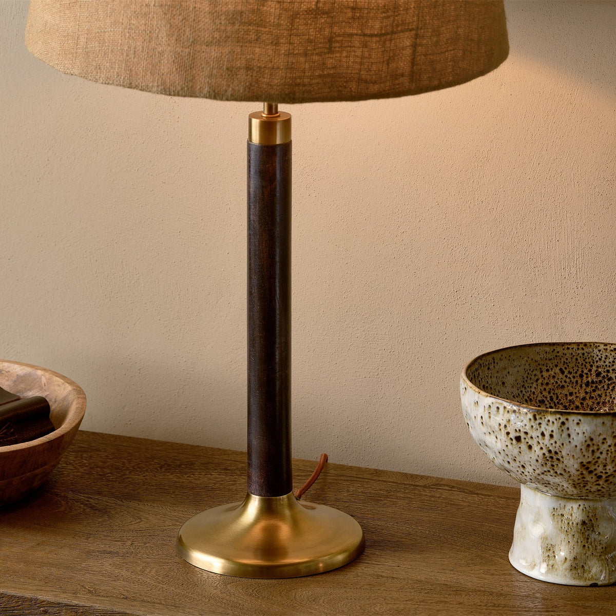 Digha Wooden Table Lamp Base in dark stained mango wood with antique brass cup and round foot, paired with a linen shade, styled on a wooden sideboard beside ceramic bowls.