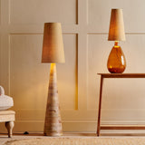 Dia Medium Jute Tall Lampshade in natural straw-coloured woven jute, shown on a tall tapered floor lamp and a glass table lamp in a living room setting.