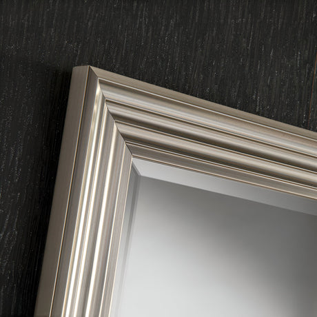 Close-up of the Deco Rectangle Wall Mirror in Silver, featuring a metallic, ridged frame against a textured dark wall. The polished silver finish enhances its modern simplicity, adding an elegant touch to the reflective surface.