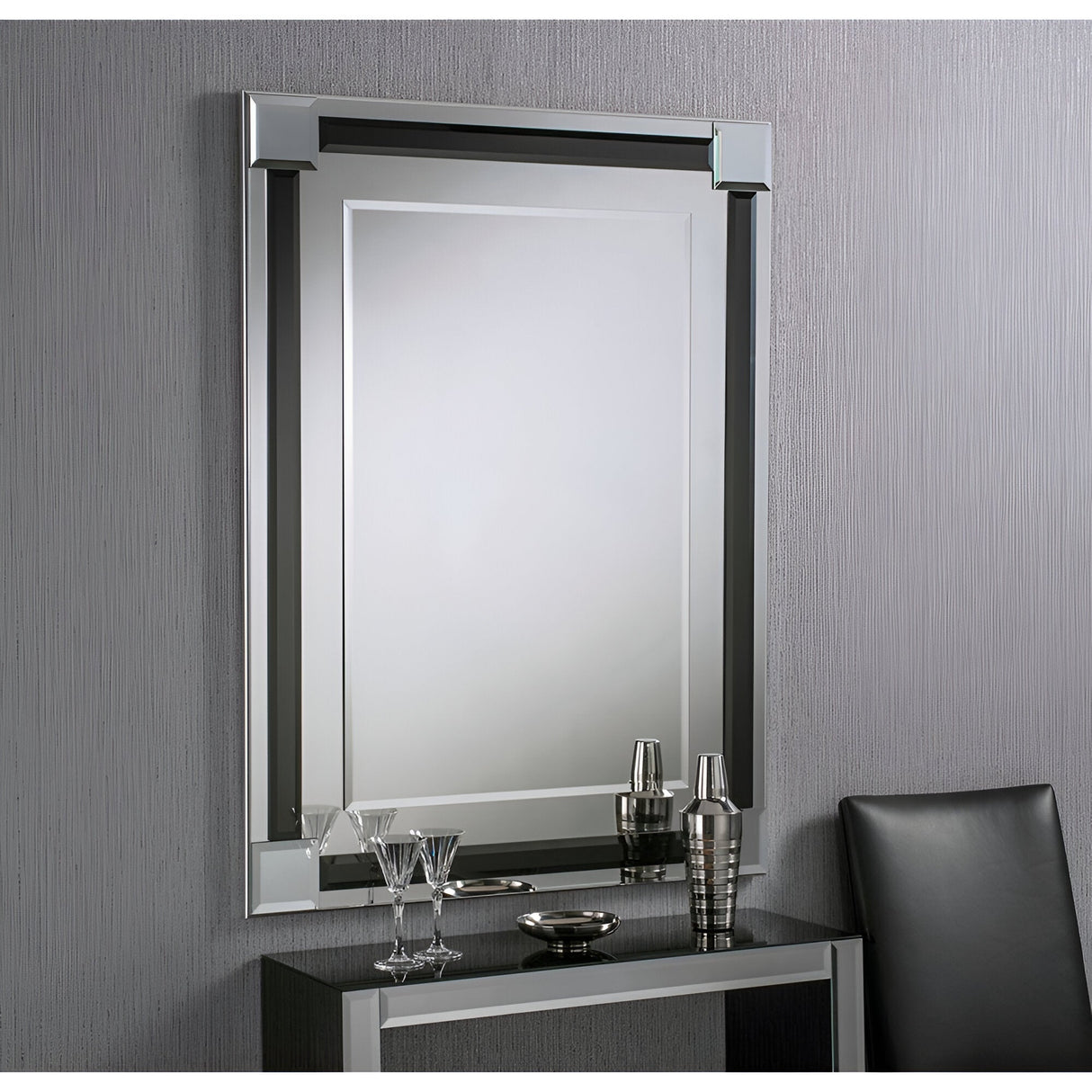 The Glowis Rectangle Wall Mirror in black, measuring 117x84cm, hangs above a sleek black console table adorned with glasses, a cocktail shaker, and a small tray. A partially visible black chair completes the setup against a textured gray wall, infusing the room with a modern touch.