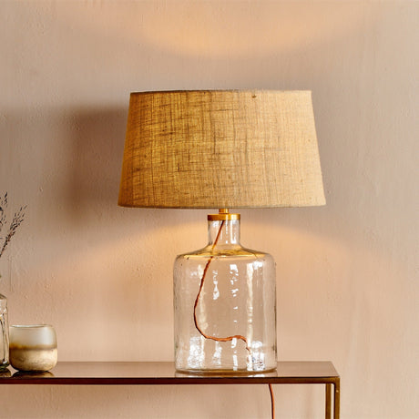 Edina Small Recycled Glass Table Lamp Base in clear hammered glass with brass neck collar, paired with a woven neutral tapered shade on a console table.