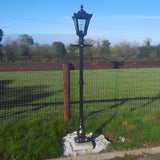 Black traditional lamp post with lantern-style top installed in a garden setting, mounted on a concrete base containing a galvanised steel 150mm square foundation frame.