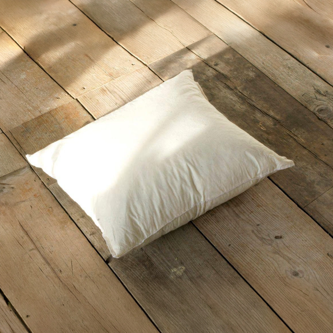 Rectangular feather cushion pad in cream cambric casing, 65 x 45cm, shown plump on a wooden floor.