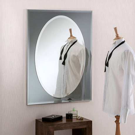 A wooden mannequin dressed in a white shirt and black tie stands in front of the Vivid Oval Wall Mirror Grey - 83x62cm. The mirror's reflection enhances the scene with a decorative touch. Beneath it, a wooden table displays a small black box and a green perfume bottle.