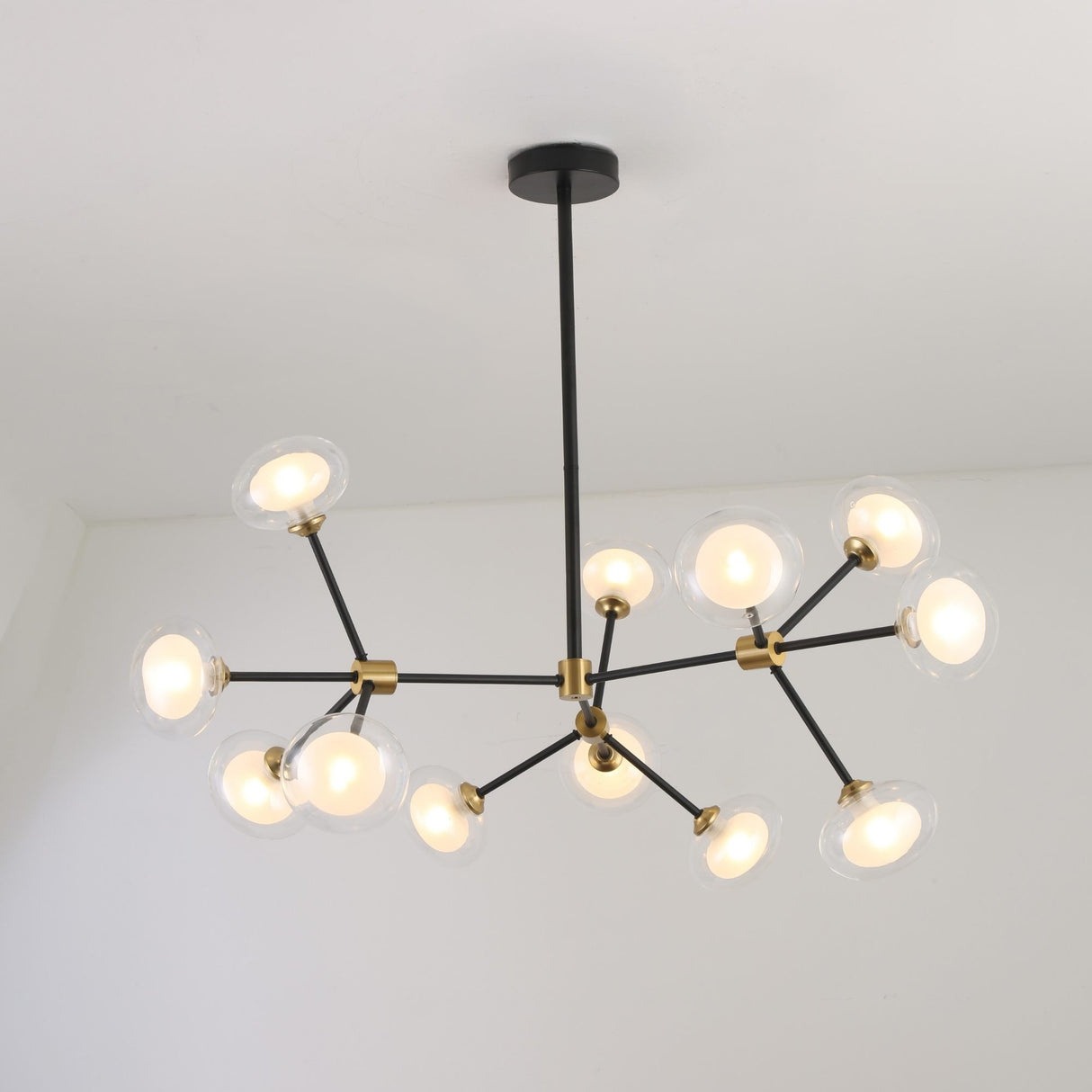 Niori Galaxy 12 Light Branching Chandelier with asymmetric matt black arms, brushed brass collars and clear glass globes, mounted to a white ceiling.
