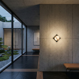 A modern minimalist interior with concrete walls, the Oblyra 1 Light Small Angled Plate Alabaster Wall Light in Soft White & Black, black tile flooring with wood accents, floor-to-ceiling windows, and views of a Japanese rock garden outside.