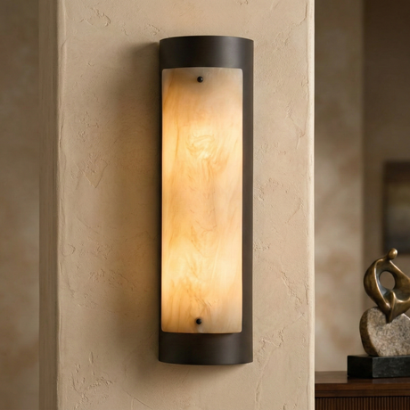 The Elantra LED Large Vertical Alabaster Wall Light in Soft White & Black features a frosted cylindrical shade and emits warm light. It's shown on a textured beige wall with abstract décor visible in the background.
