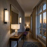 Elegant hotel room with a desk, mirror, Veradex 1 Light Alabaster Block Table Lamp in brass & soft white, large windows, beige curtains, and a sunset view of Paris featuring the Eiffel Tower in the distance.