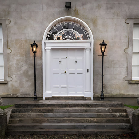 Victorian cast iron lamp post in black, 2.3m tall with tapered lantern head, shown lit beside a white panelled front door on a stone-pillared entrance.