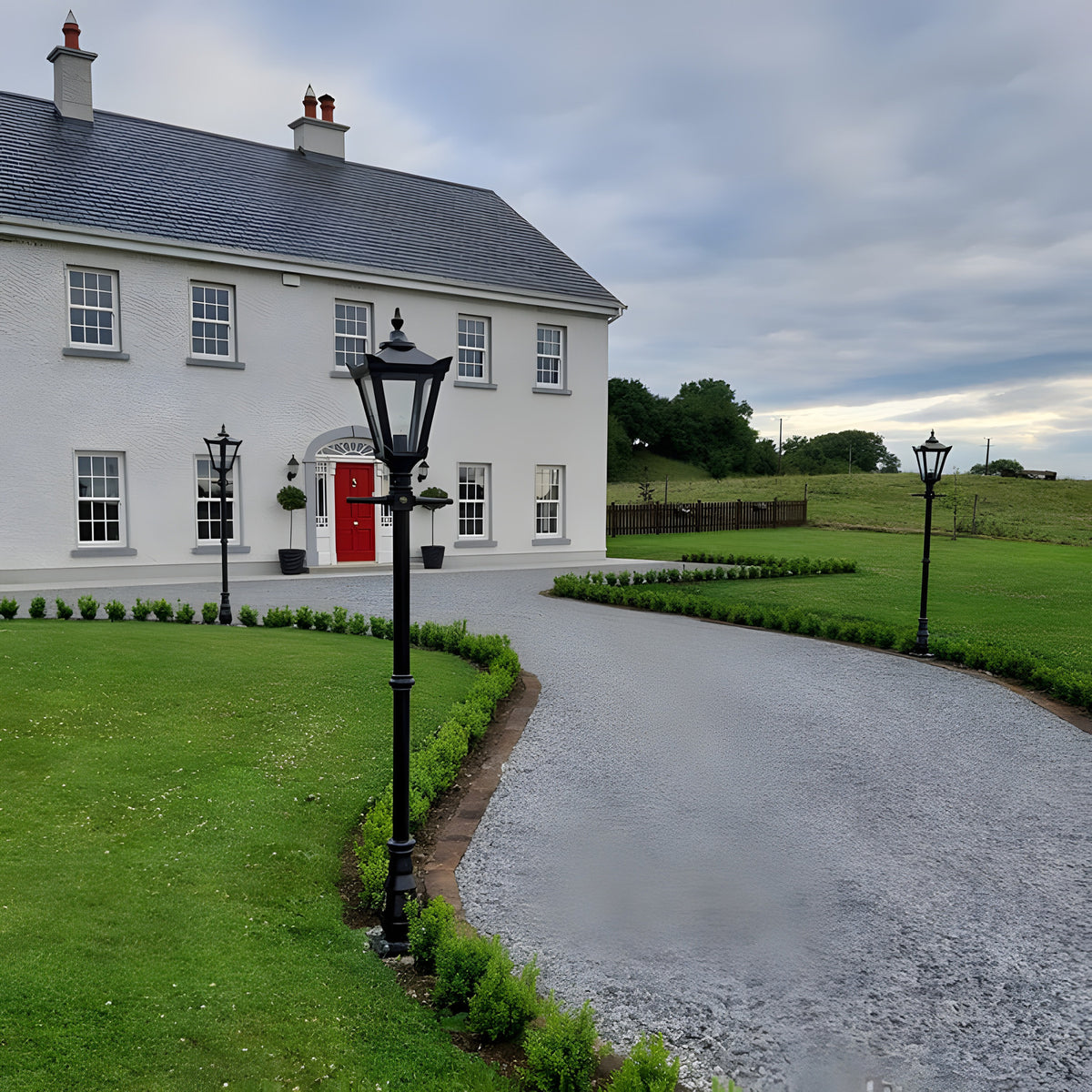 Victorian Cast Iron Lamp Post 2.3m in black, tapered four-sided lantern head on a tall post, lining a gravel driveway beside a white house.