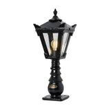 Small Victorian cast iron pedestal post light in black, tapered four-sided lantern head with stepped crown and finial, glass panels, single E27 bulb, on a white background.