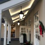 Large Victorian cast iron hanging lanterns in black, tapered four-sided heads with stepped crowns, suspended on chains under a covered porch entrance.