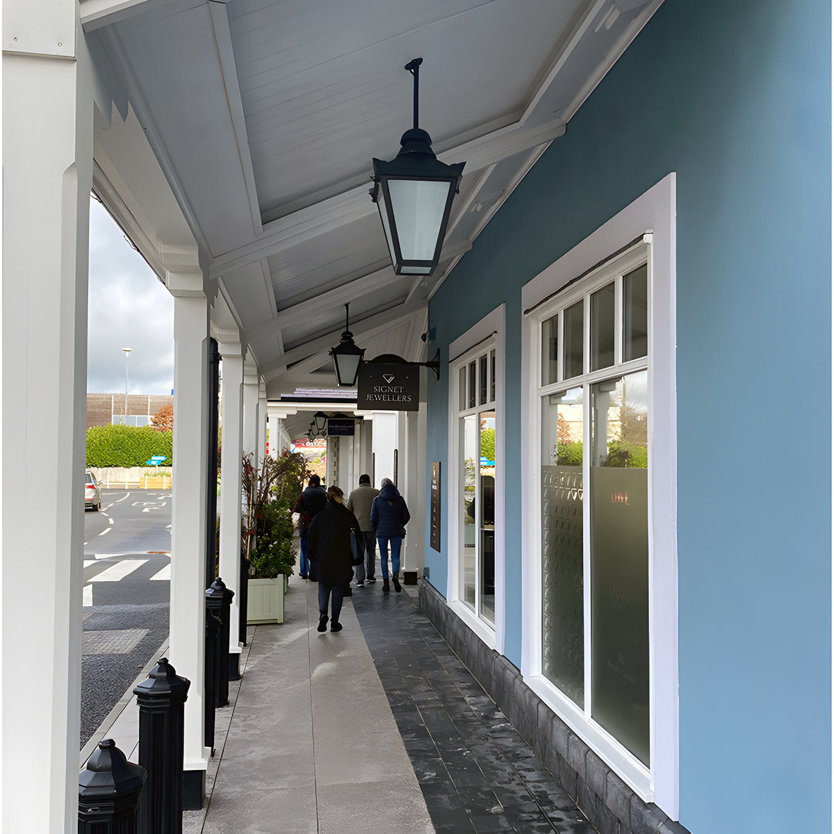 Large Victorian cast iron hanging lantern in black, tapered four-sided head with stepped crown, shown mounted on a covered shopfront walkway ceiling.