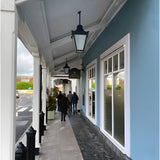 Large Victorian cast iron hanging lantern in black, tapered four-sided head with stepped crown, shown mounted on a covered shopfront walkway ceiling.