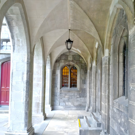 Medium Victorian cast iron hanging lantern in black, tapered four-sided glass head on a chain, shown suspended in a stone archway walkway.